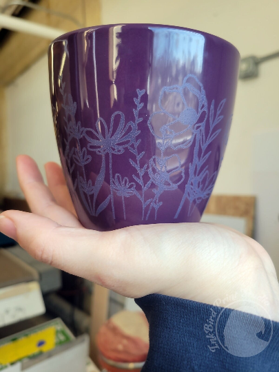 Glossy purple ceramic planter pot laser etched with intricate botanical designs; hand-held in workshop.