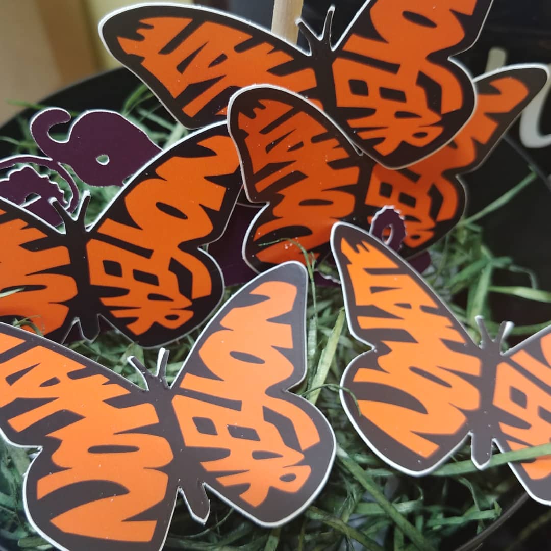 Several orange and black butterfly-shaped signs with the word “VOTER” arranged on green artificial grass. The signs overlap and are grouped closely together.