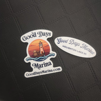 Two vinyl die-cut stickers: one shows a marina sunset with lighthouse, other is oval, both say Good Days Marina, Houghton Lake, MI.