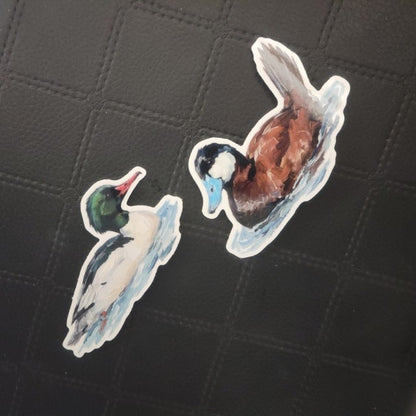 InkBird Print Studio vinyl duck stickers—one mallard, one blue-billed teal—on a stitched textured black background. Printed for Good Days Marina