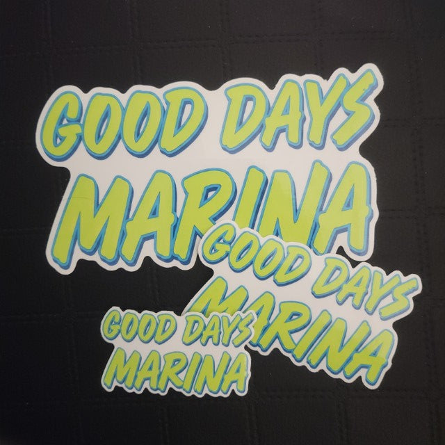 Premium vinyl GOOD DAYS MARINA die cut stickers in blue and green, assorted sizes, slightly overlapping on black textured surface. 