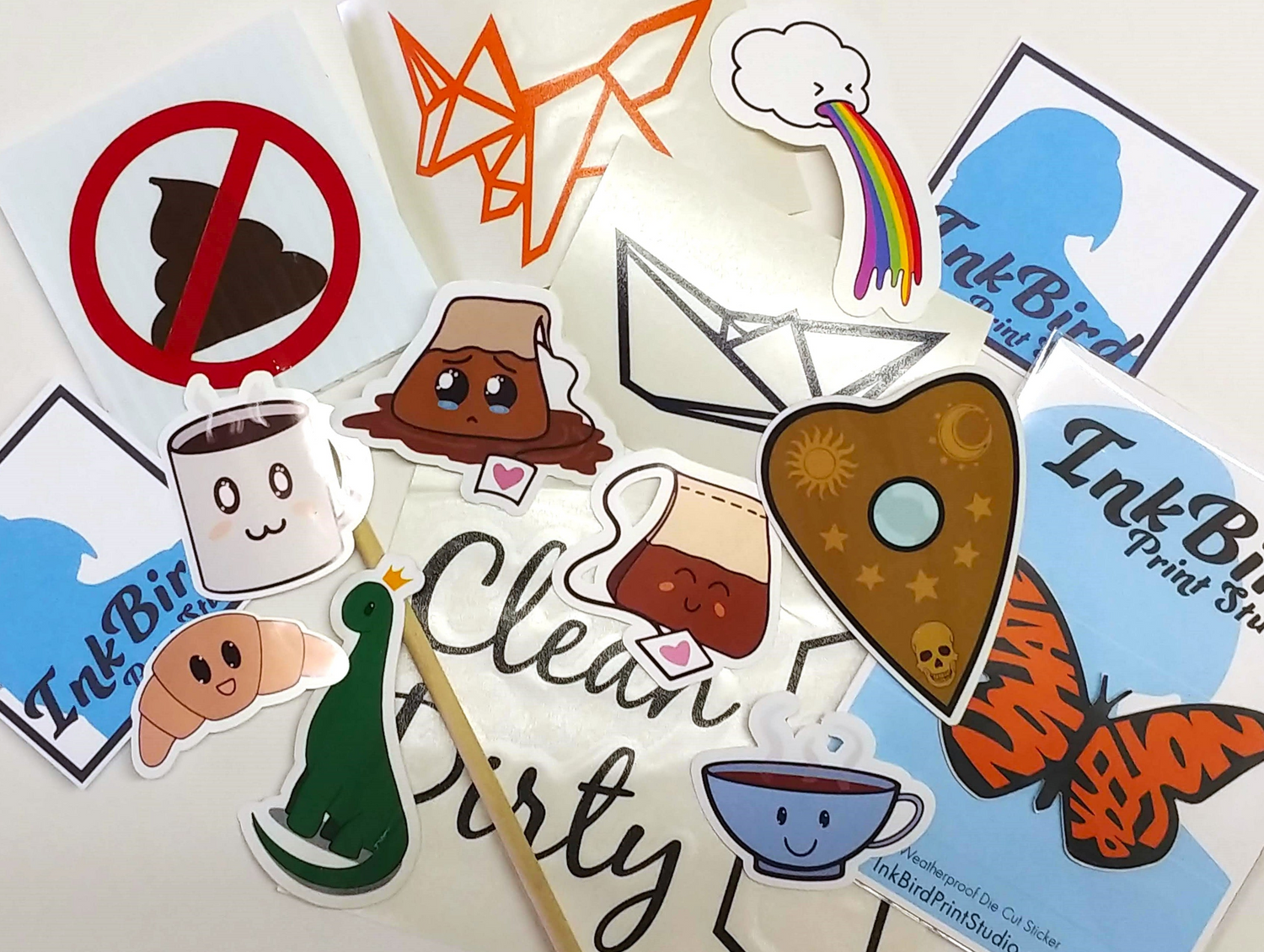 Handmade vinyl stickers in bright colors, featuring coffee cups, a dinosaur, croissant, emoji icons, and a Clean/Dirty sign.