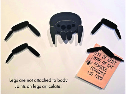 Laser-etched black wood spider magnet with bendable jointed legs, neodymium base, plus pink potion ingredient card—unique fridge decor.